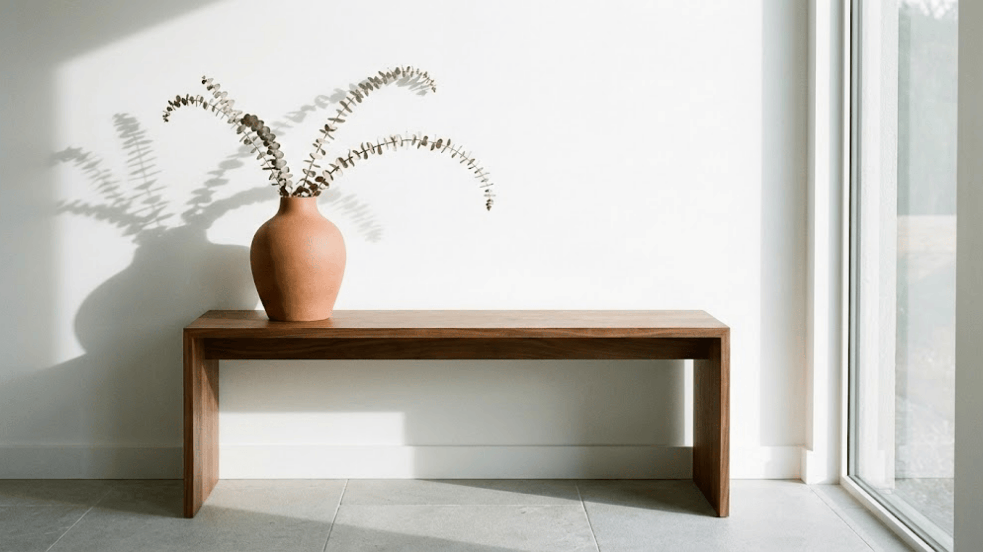 minimalist walnut console with single terracotta vase and dried eucalyptus against white wall