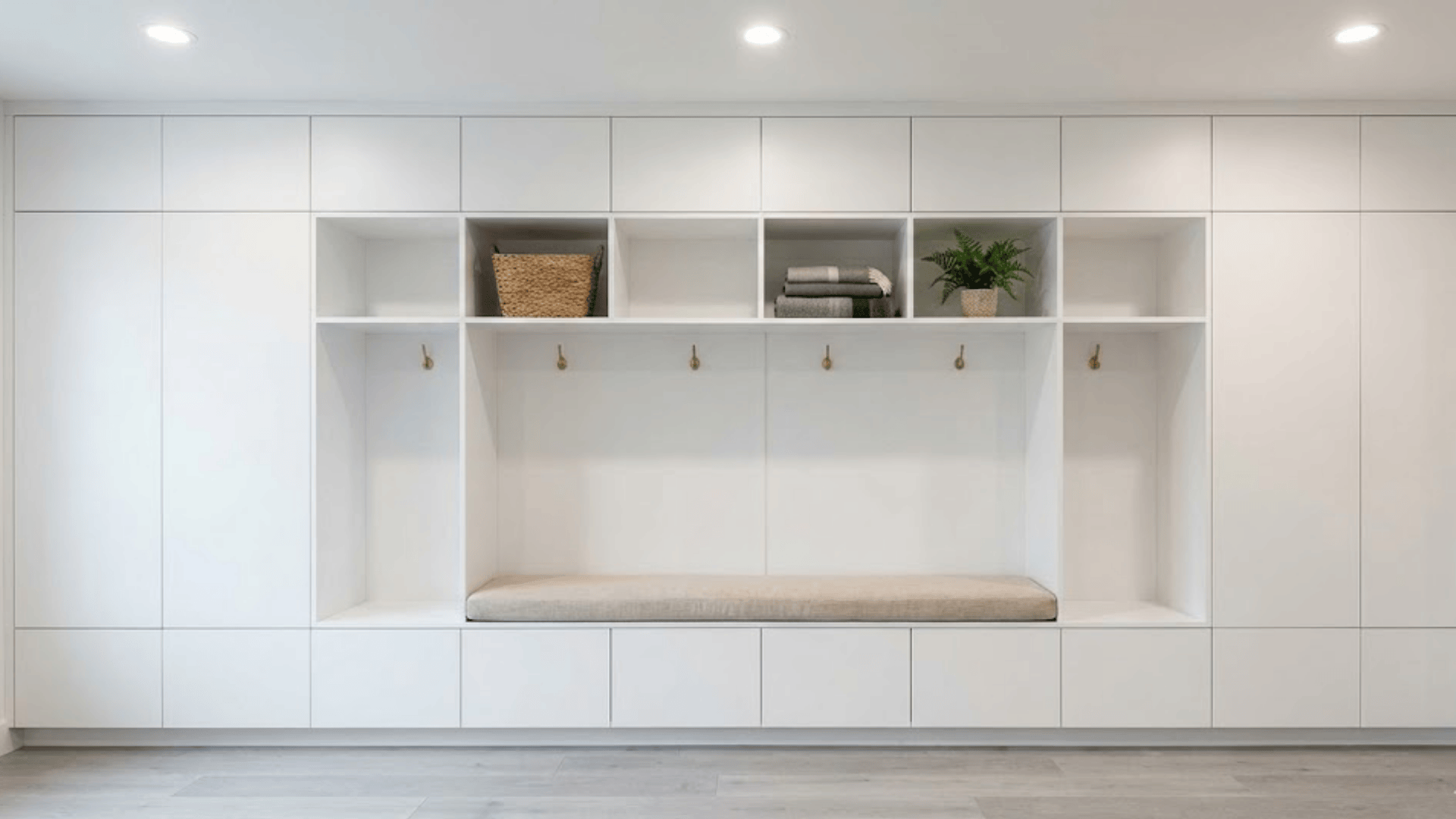 floor to ceiling white built-in storage wall with mix of open cubbies closed cabinets and bench seat