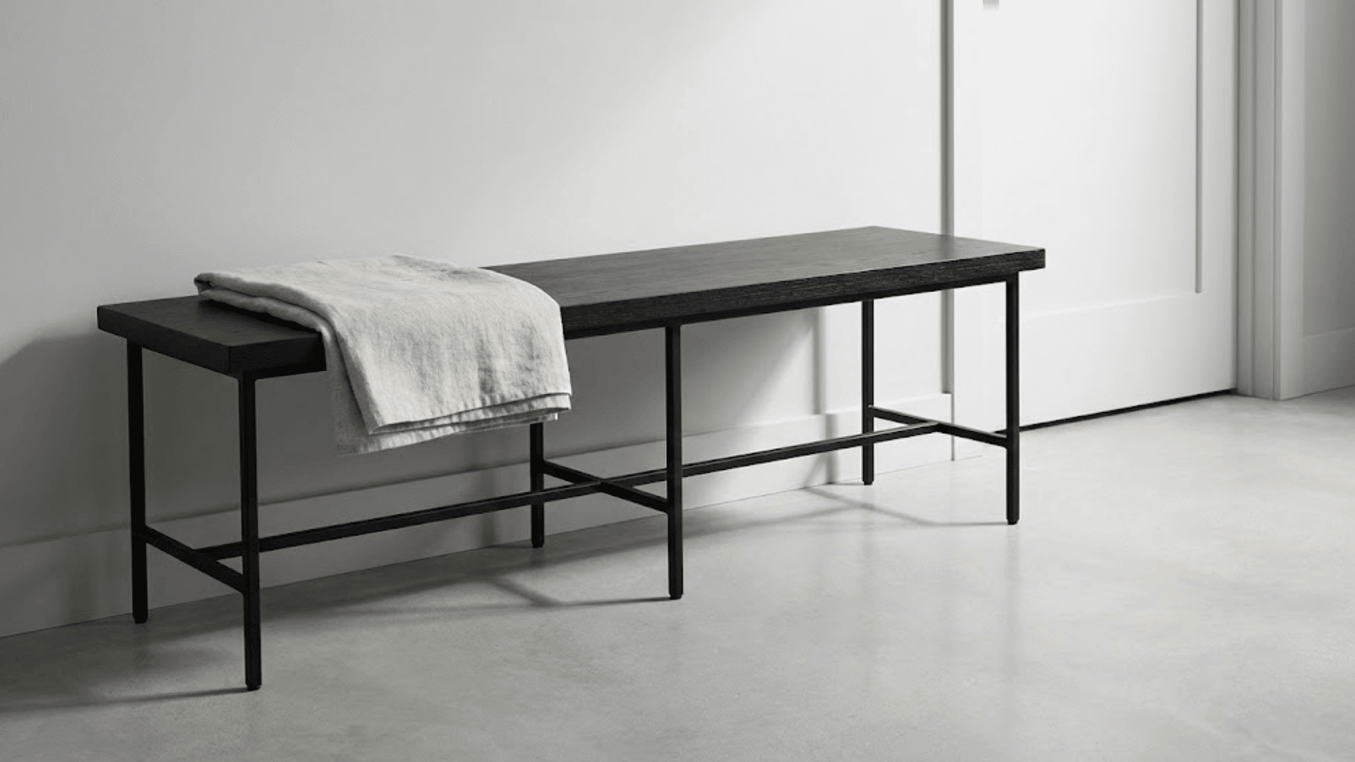 low profile black oak bench with thin metal legs and clean geometric lines in modern entryway
