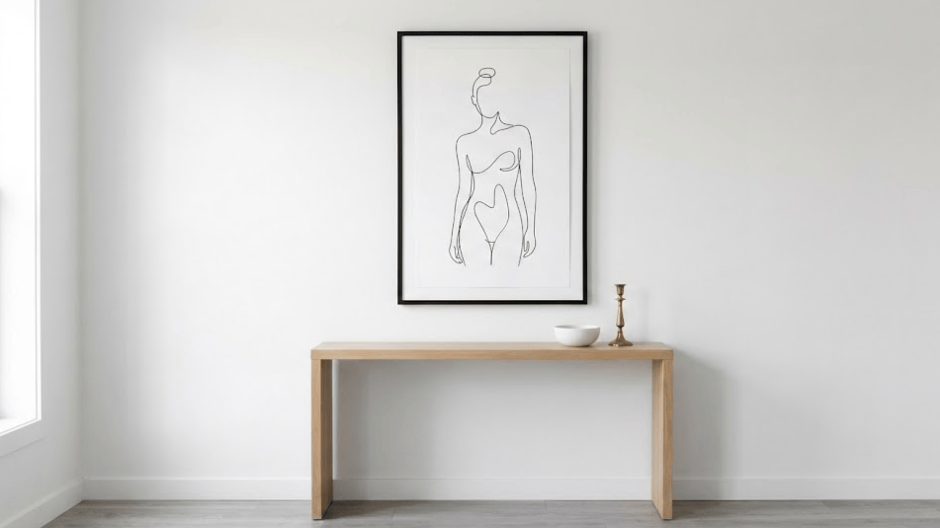 minimal black line art drawing in thin frame showing abstract figure on white wall above console
