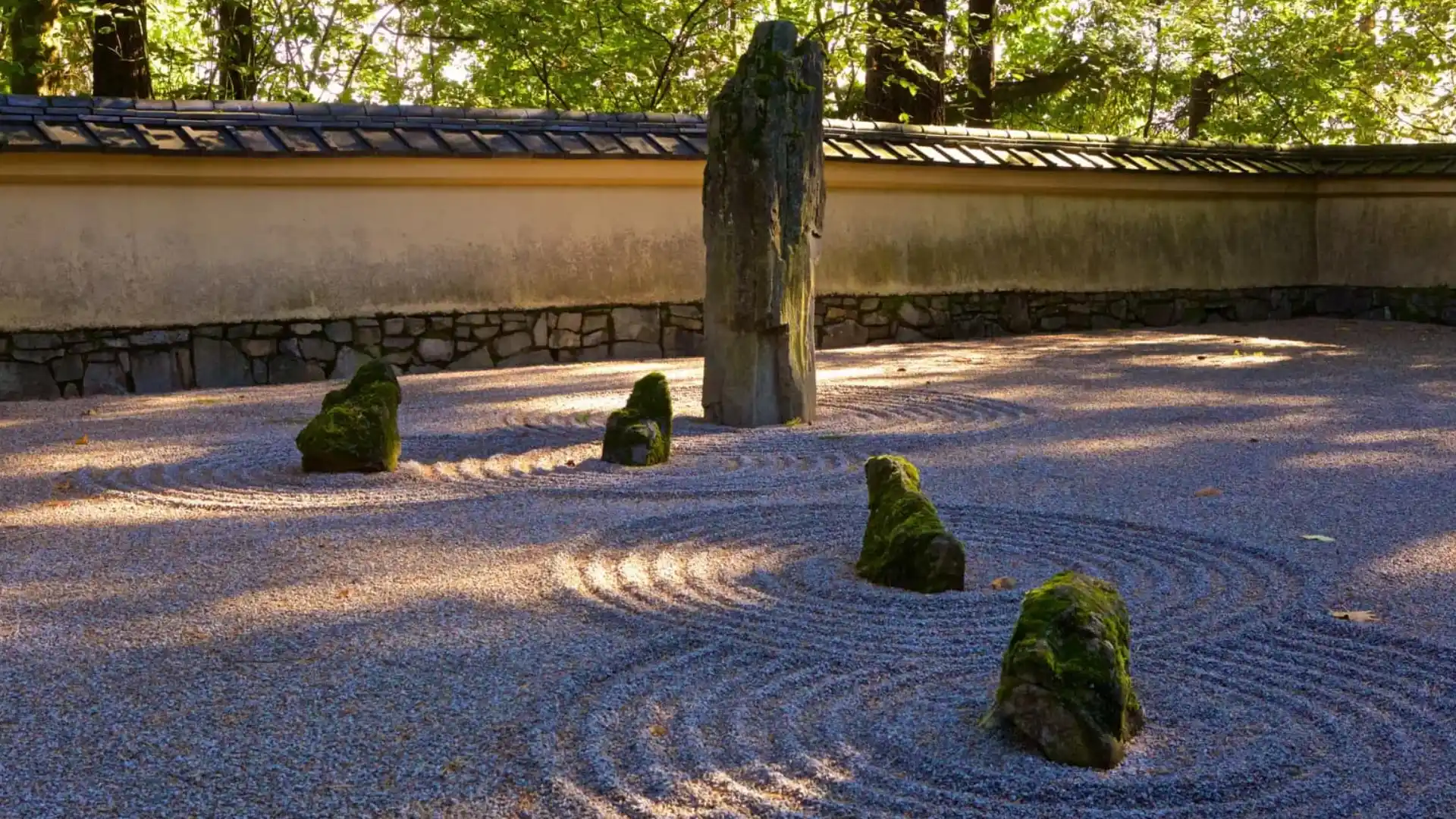 japanese rock garden with raked gravel moss covered stones and a tall standing rock beside a garden wall