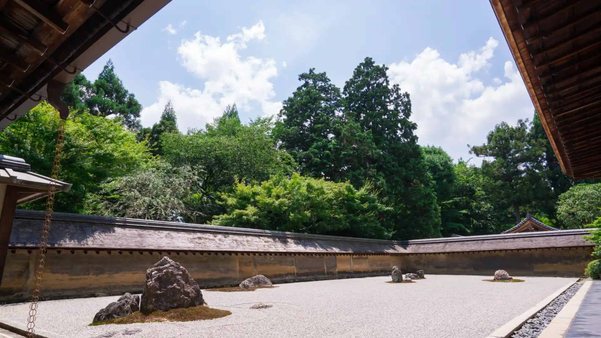 ryoan ji rock garden with raked white gravel stone groups temple walls and lush trees under blue sky
