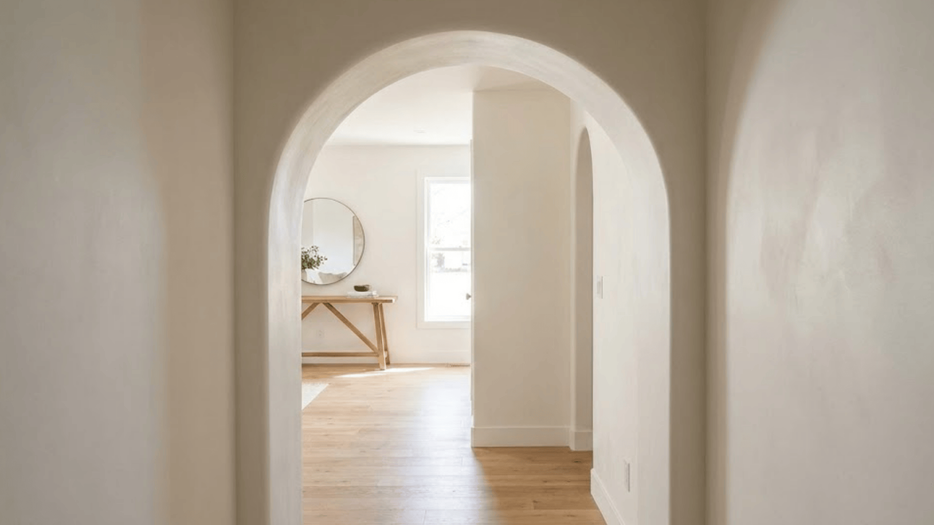 soft arched doorway with curved top painted white leading to console and mirror in entryway beyond