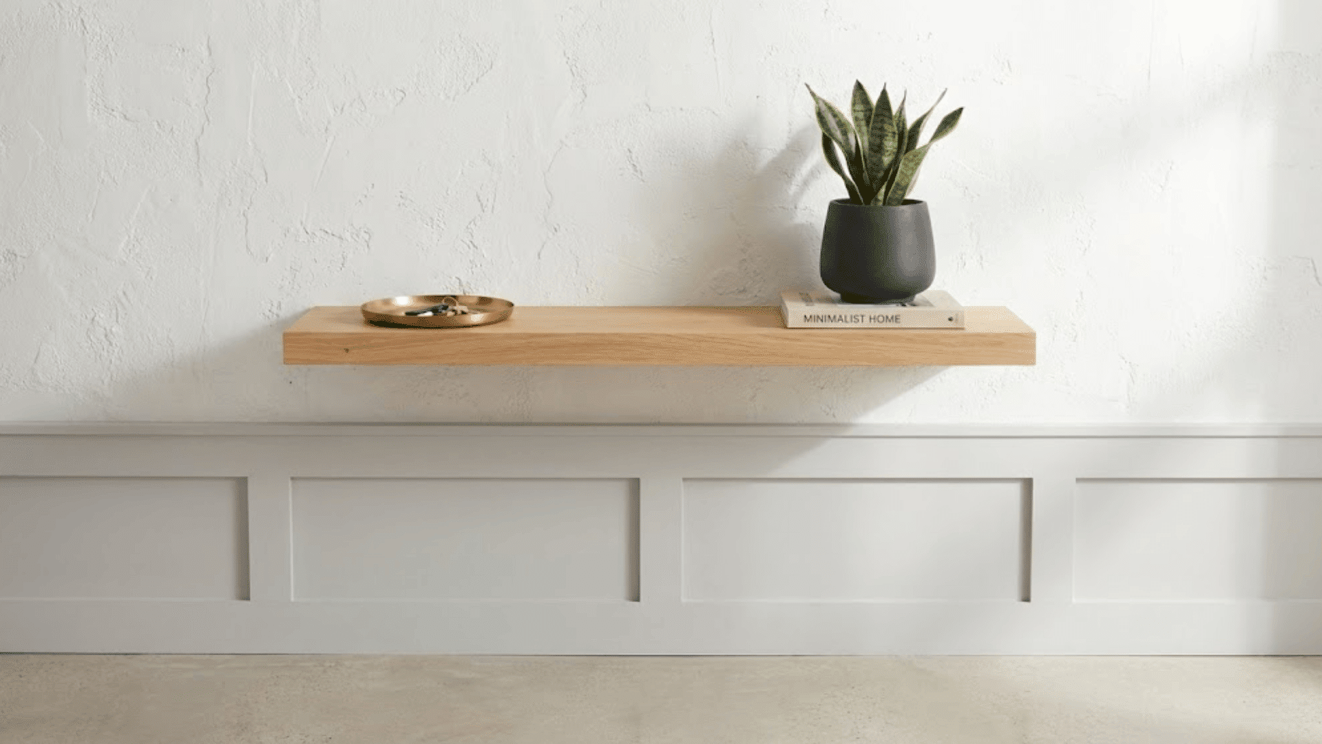 slim wall-mounted oak shelf on white wall holding keys plant and book in minimalist entryway design