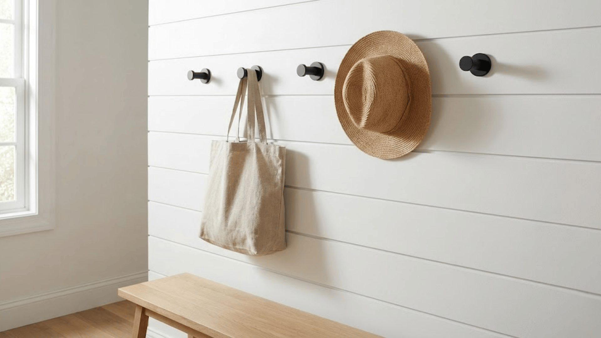 row of five matte black wall hooks mounted horizontally on white shiplap with hanging bag and hat