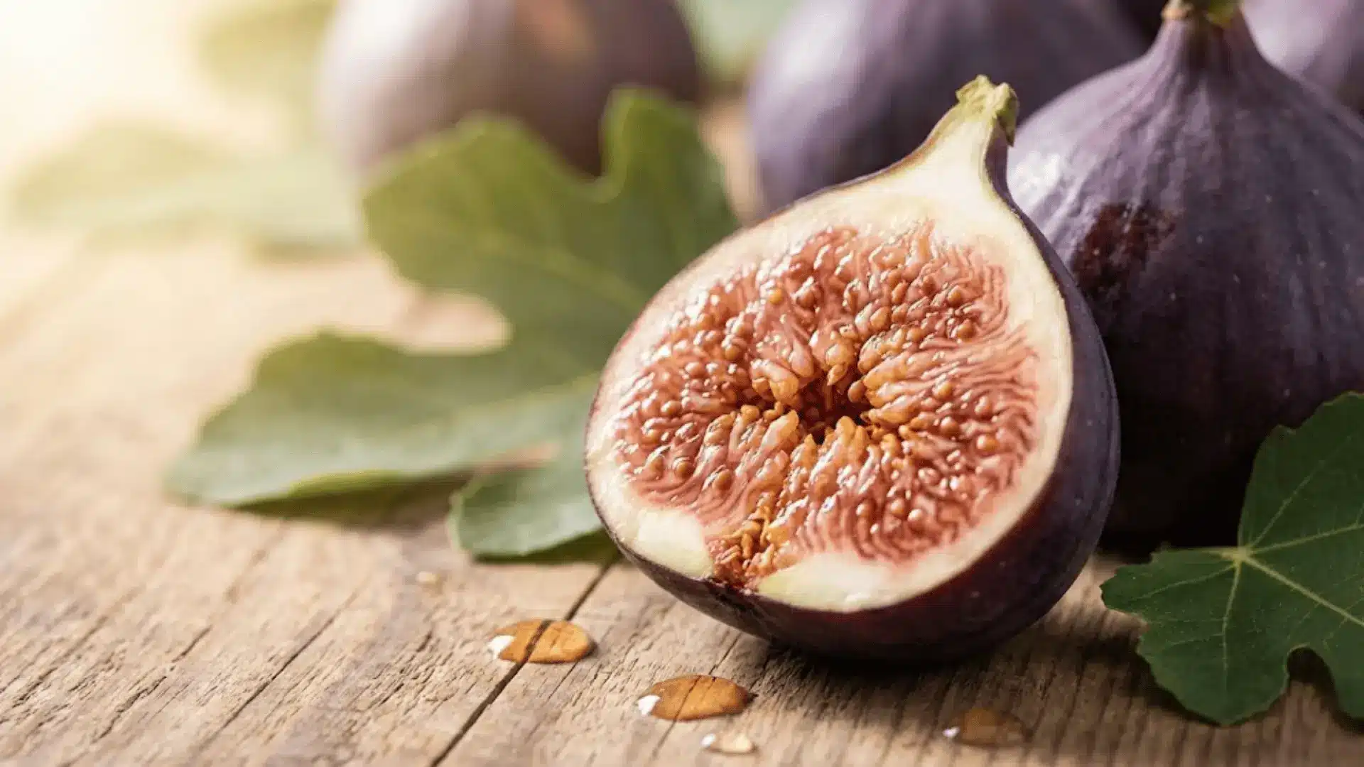fresh purple fig cut in half showing seeds and internal structure on wooden surface with natural lighting
