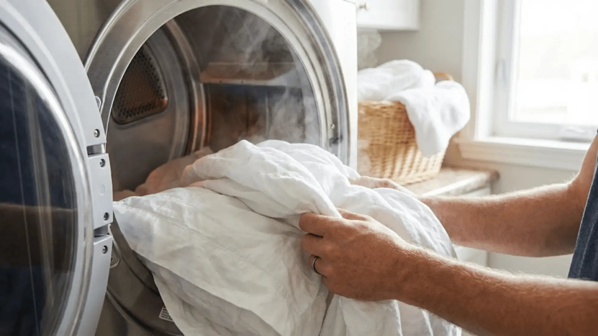 hands pulling warm white bedding from dryer drum after high heat cycle in natural light
