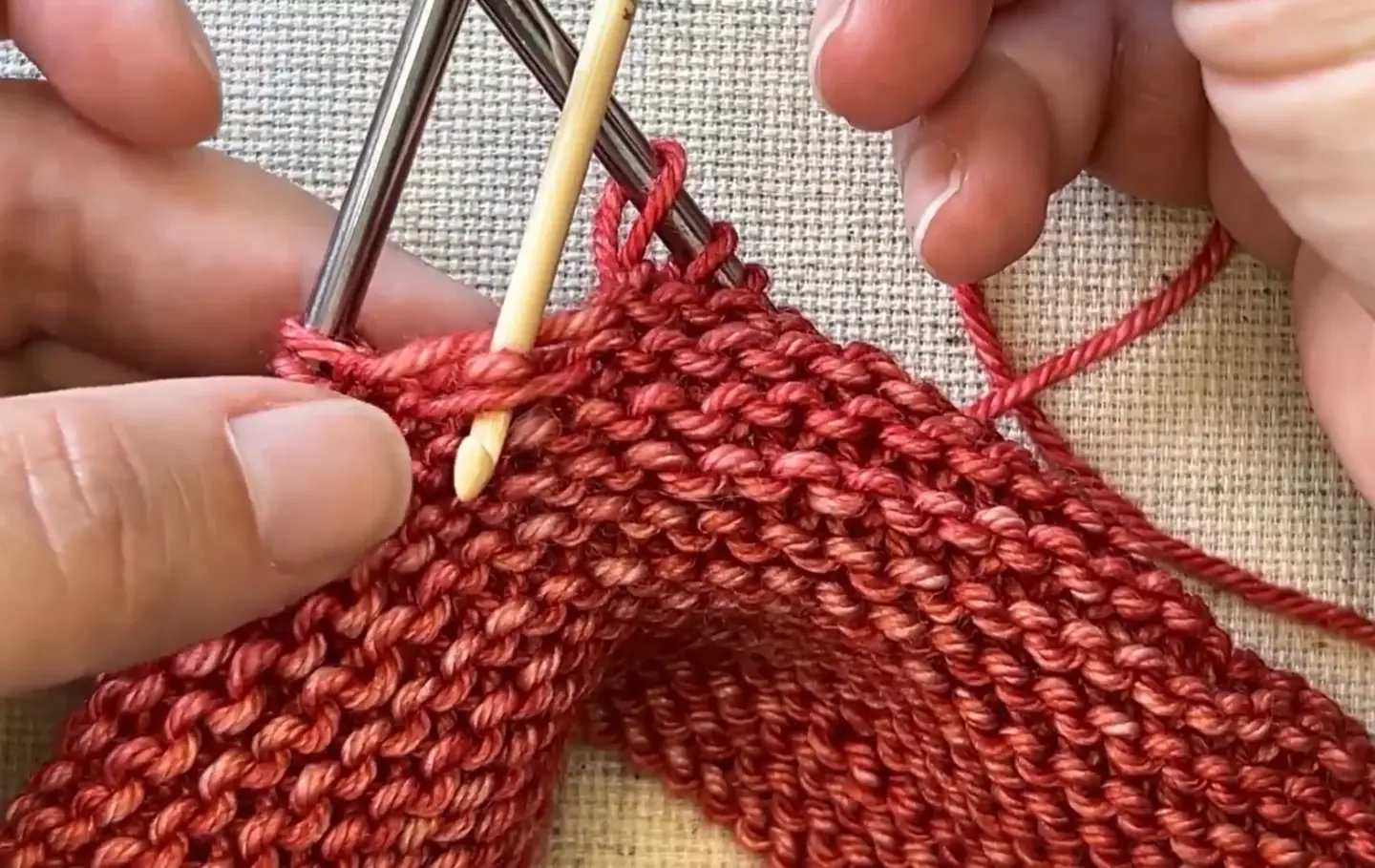 Knitting project with red yarn and needles on textured surface