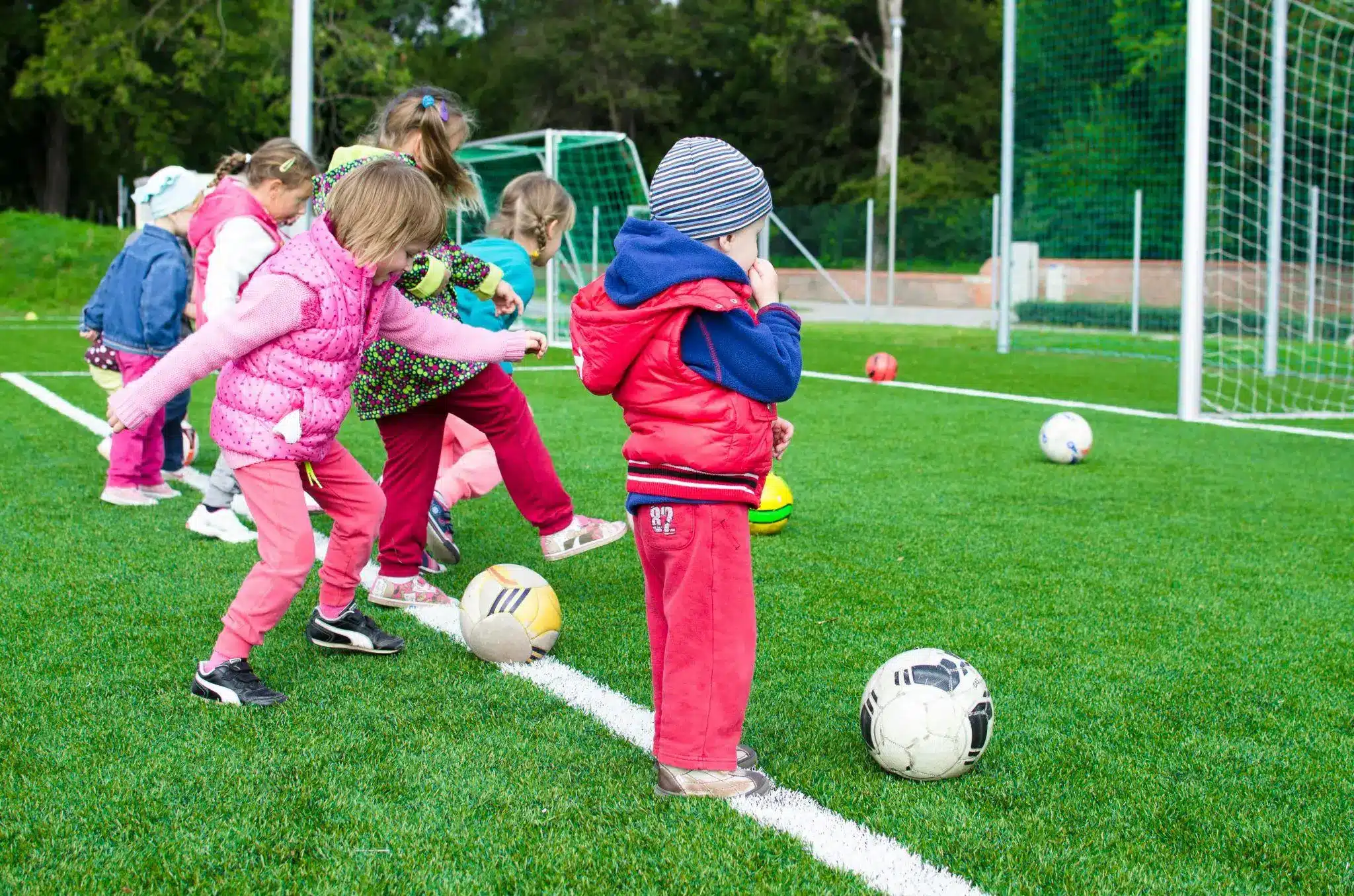 Children playing with soccer balls on a green field in colorful clothing