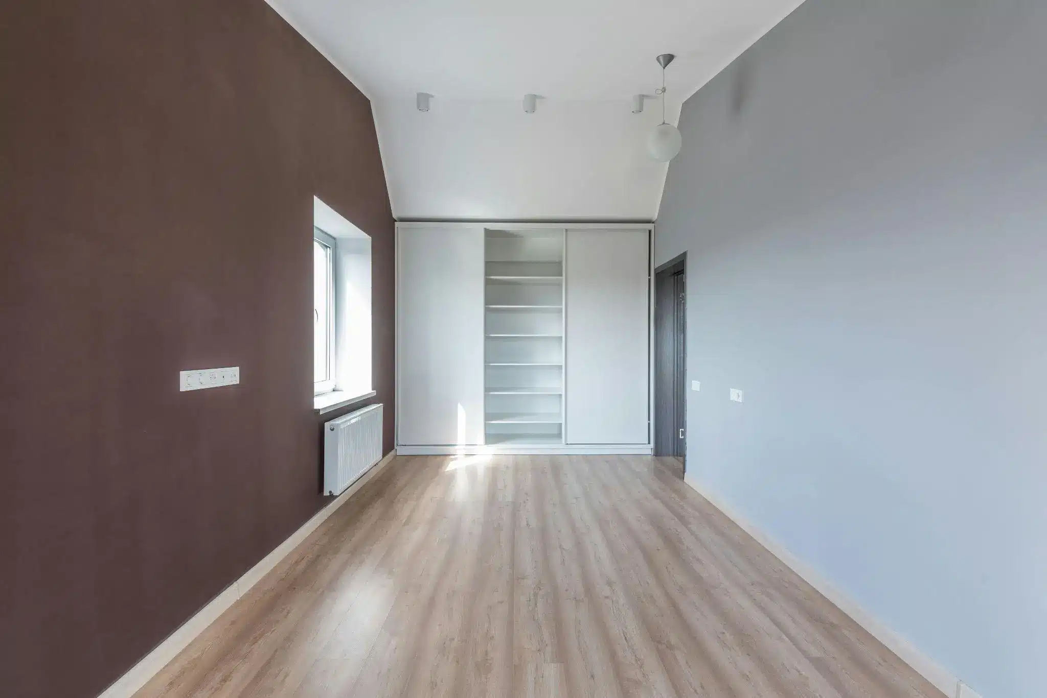 Empty room with wooden floor, brown and gray walls, and built-in white shelving unit