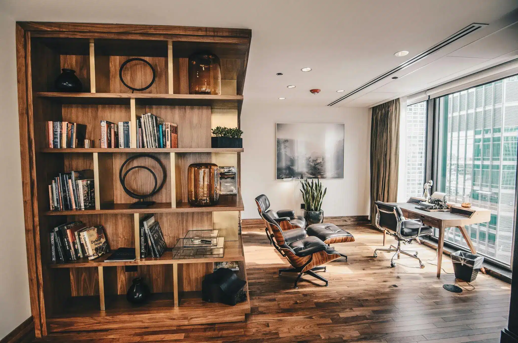 Modern office with wooden bookshelf, Eames chair, desk, and large window with city view