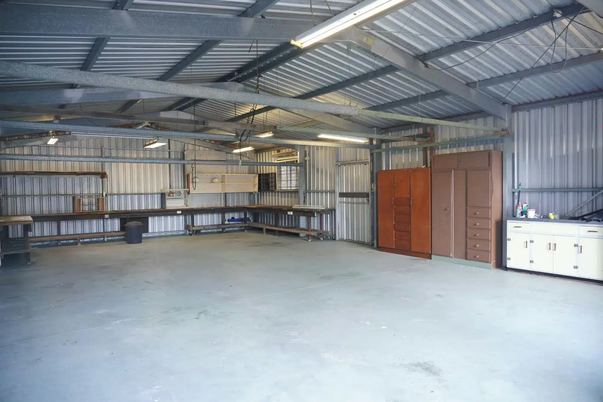 Metal garage interior with workbenches and storage cabinets under fluorescent lighting