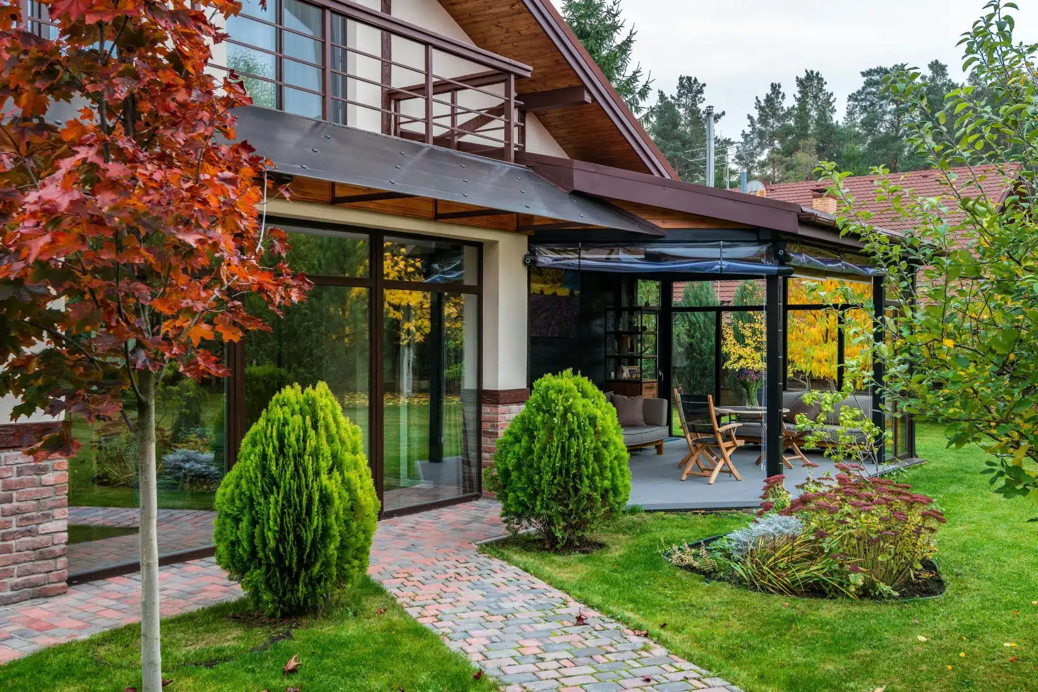 Modern house with outdoor patio, red and green foliage, glass doors, and brick pathway in backyard garden
