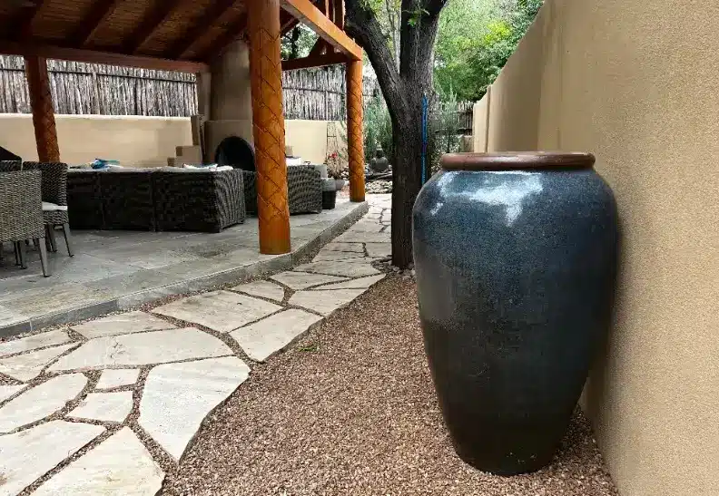 Large ceramic urn beside stone patio with wicker furniture under wooden pergola