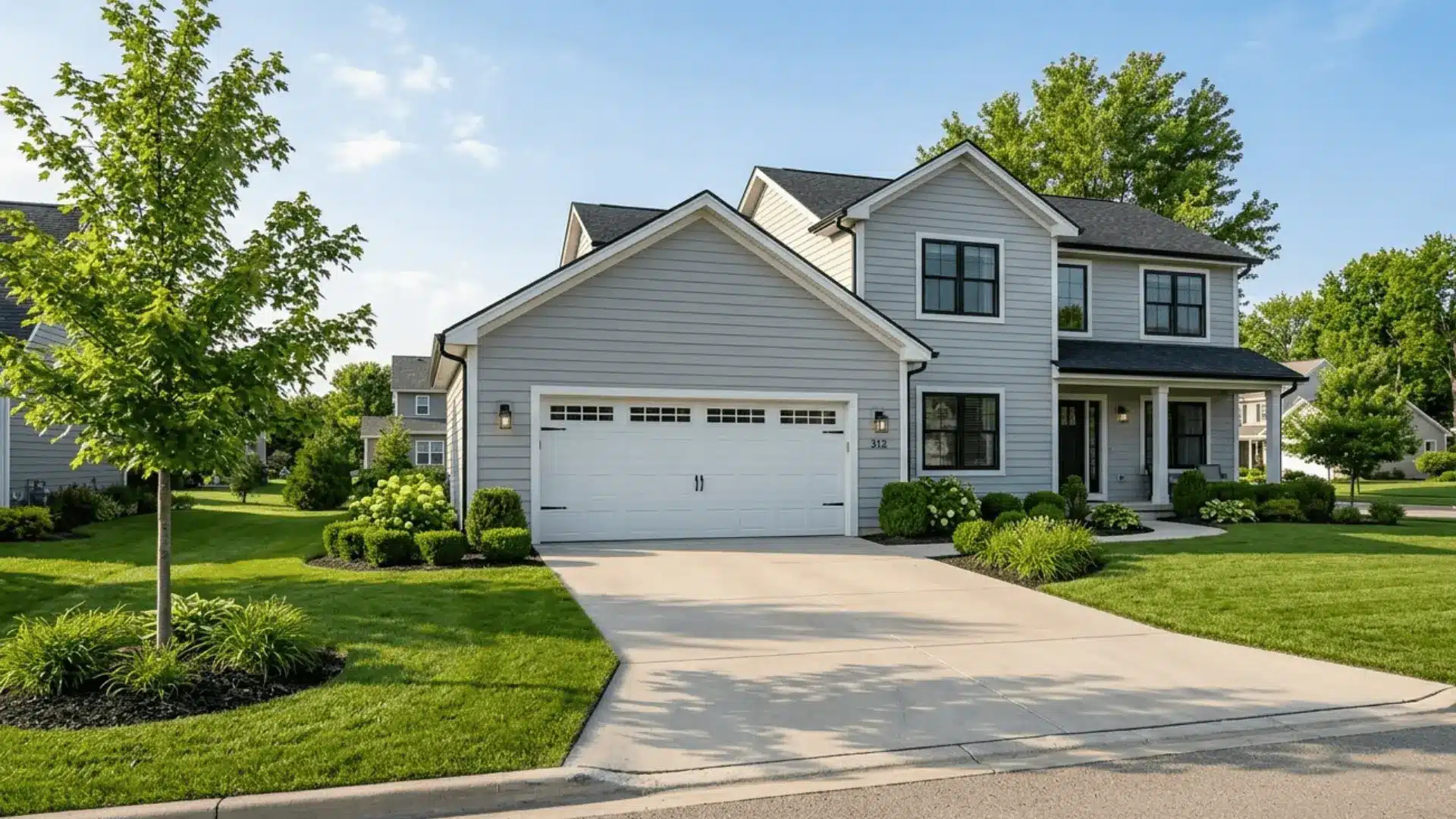exterior view of a modern attached garage with white door, grey siding, and concrete driveway on a sunny day