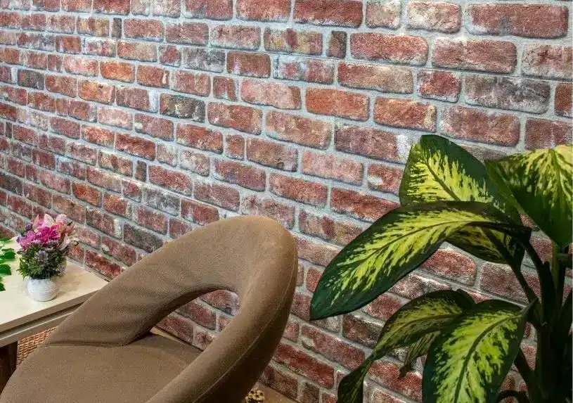 Beige chair and vibrant green plant against red brick wall with small side table and flowers