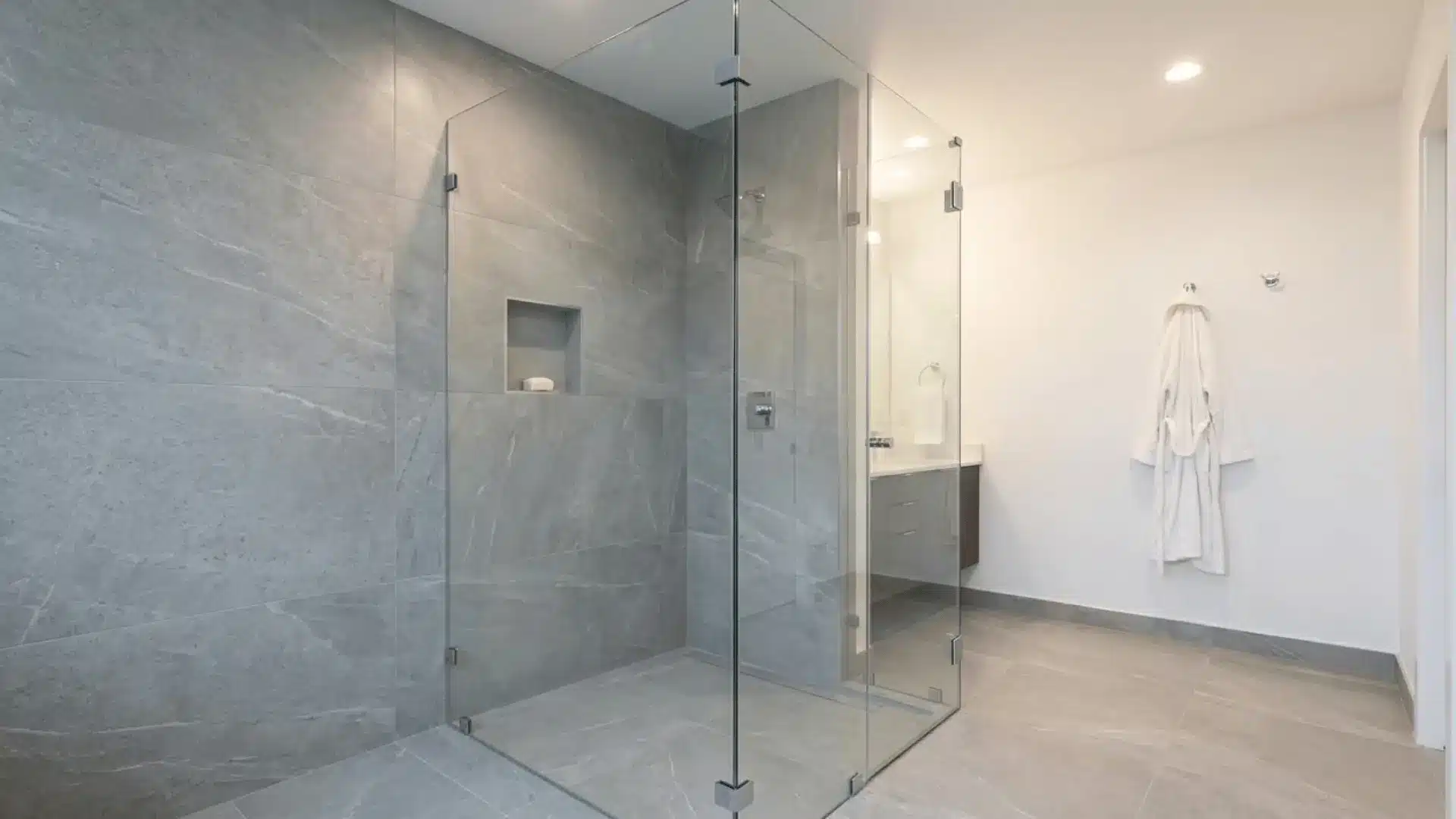 frameless glass shower enclosure with grey porcelain tiles and chrome hardware in modern bathroom