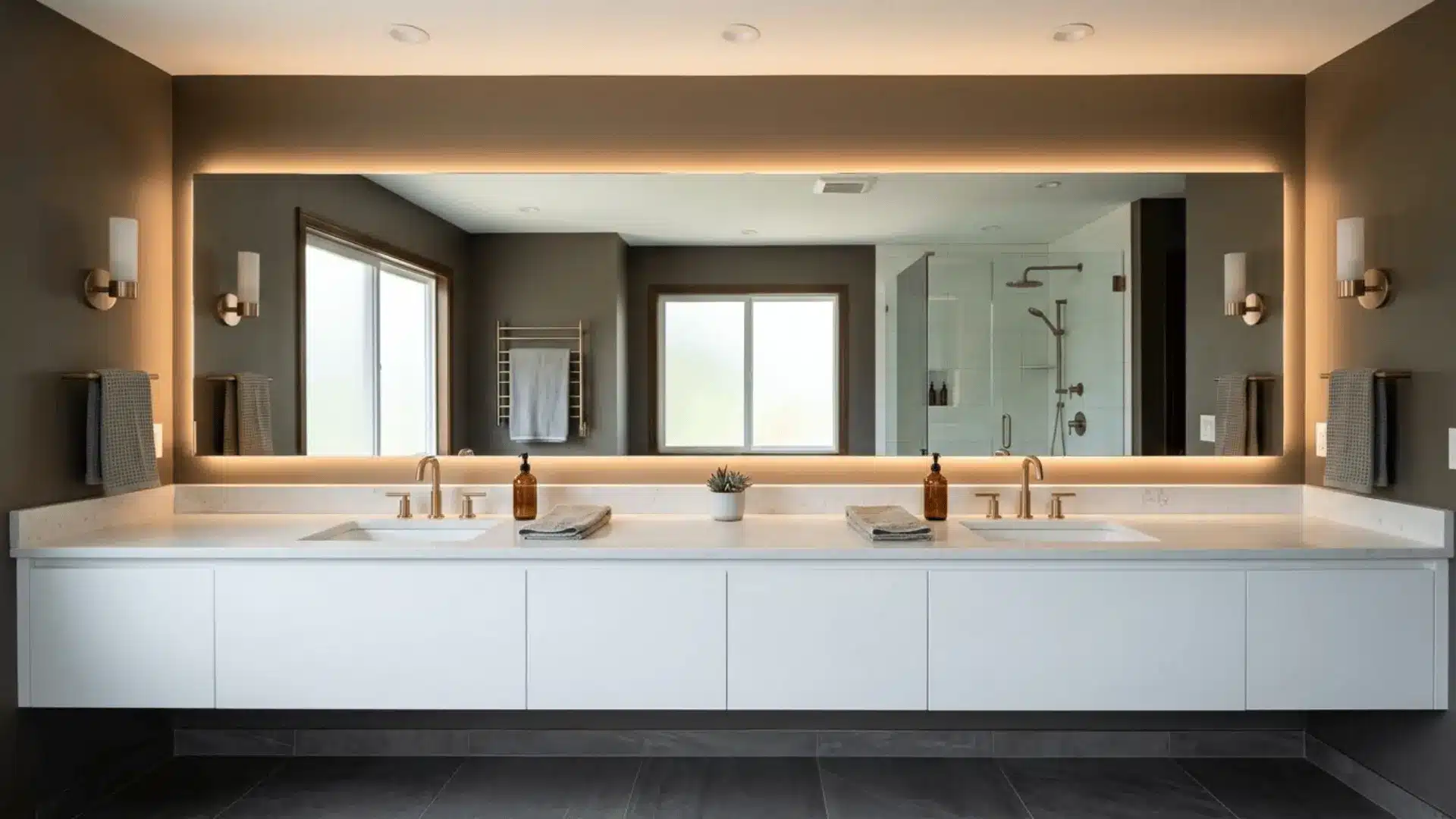 full width backlit frameless mirror above double vanity with warm led glow and brass fixtures