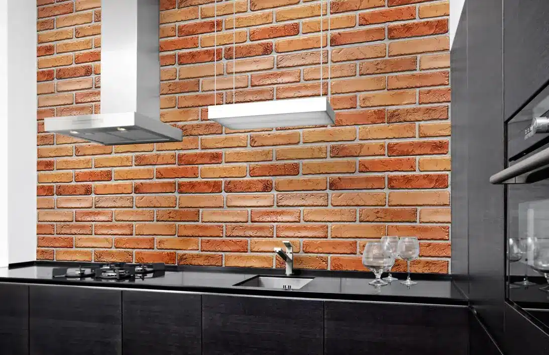 Modern kitchen with black cabinets, stainless steel hood, and exposed brick backsplash