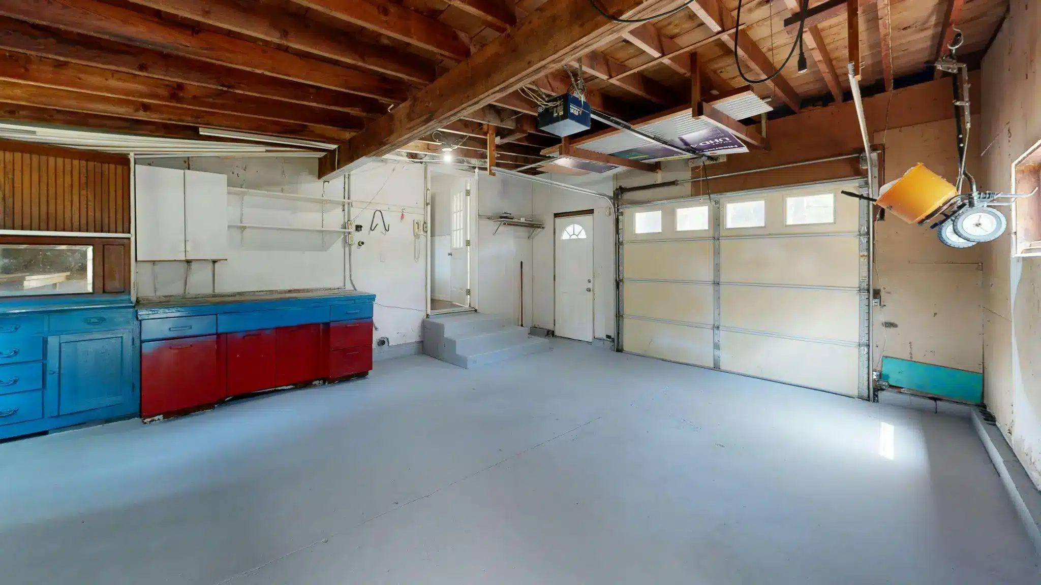 Spacious garage with wooden ceiling beams and red and blue cabinets along one wall