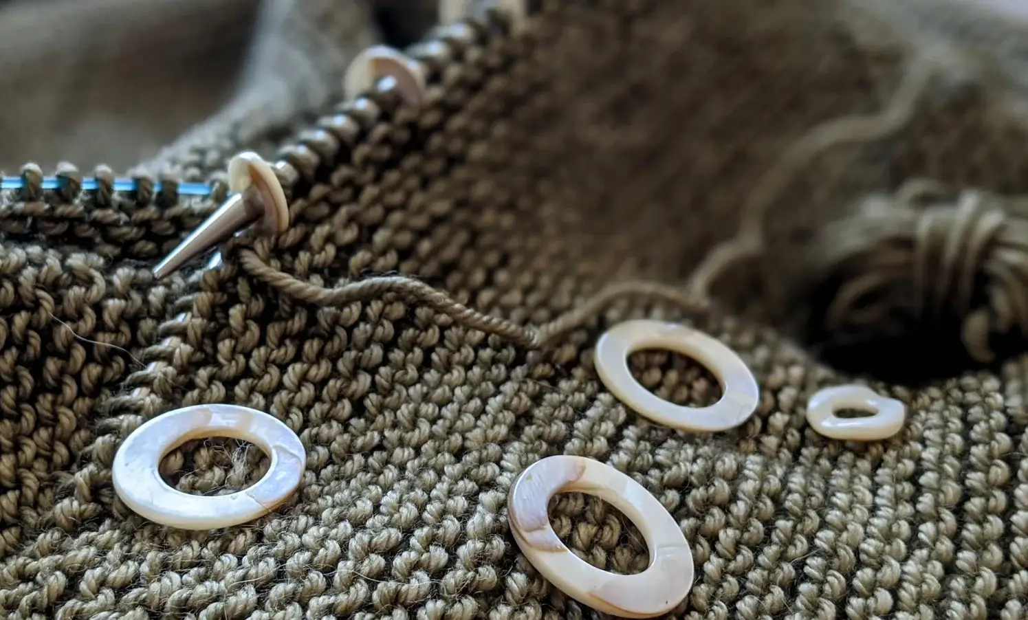 Knitting needles and beige yarn with white stitch markers on textured fabric