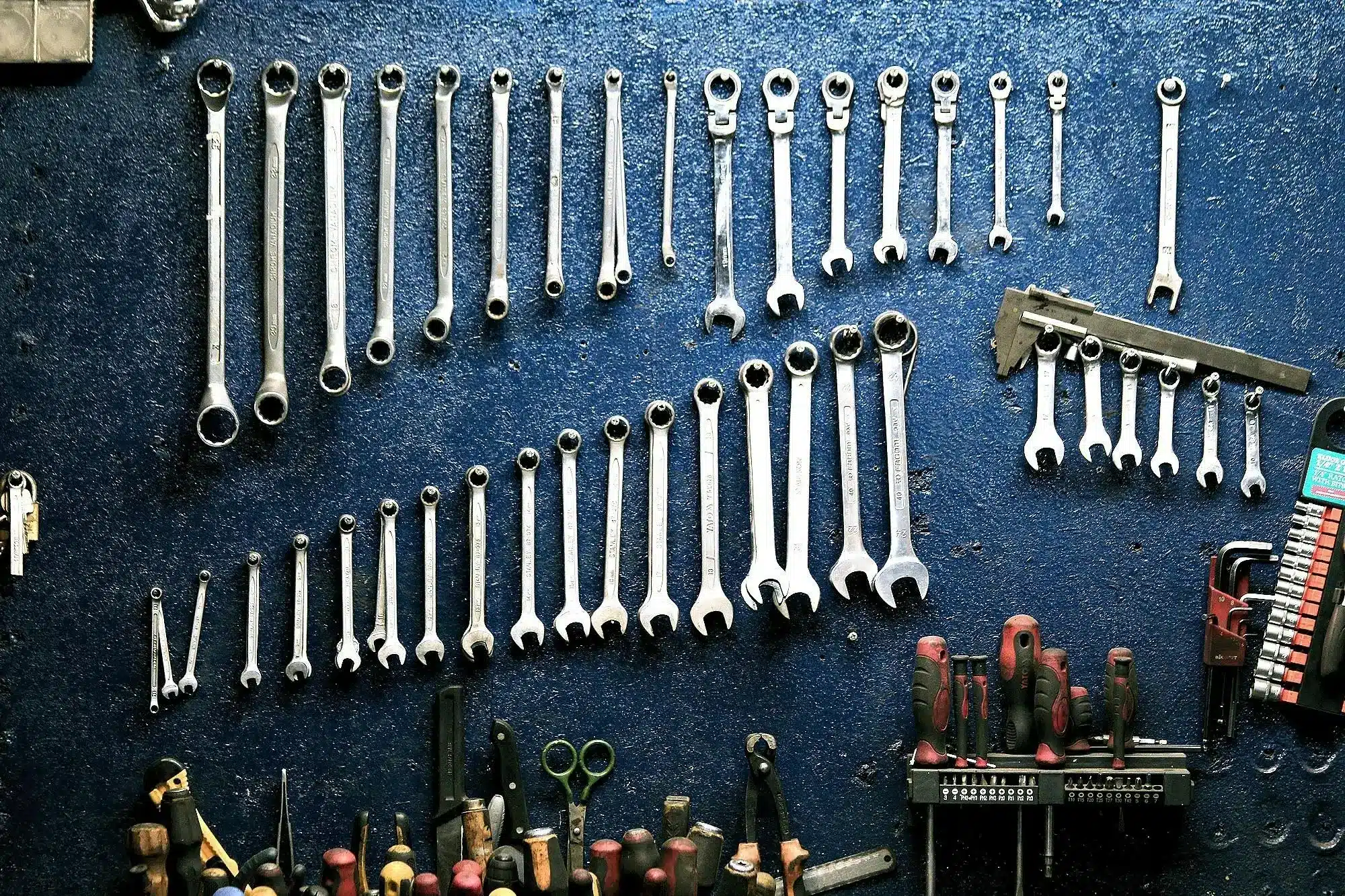 Assorted wrenches and tools neatly arranged on a blue workshop wall