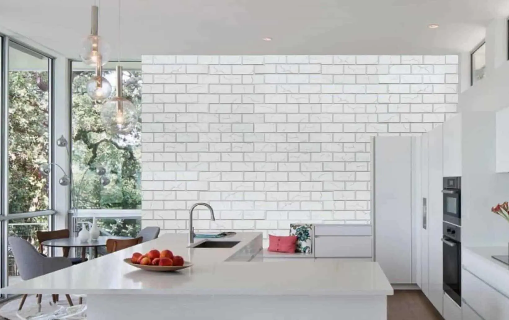 Modern white kitchen with marble backsplash, island counter, and pendant lights near large windows