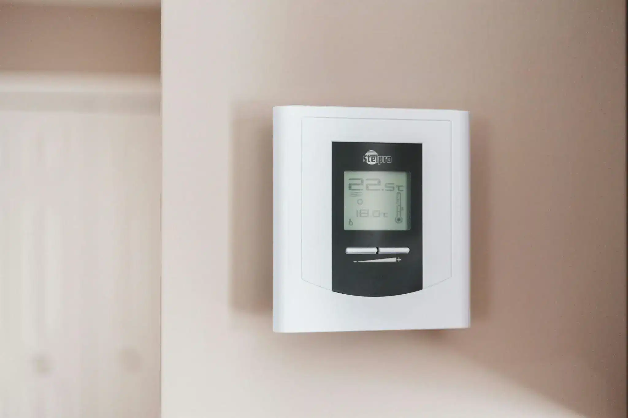 Digital thermostat mounted on beige wall displaying temperature settings indoors