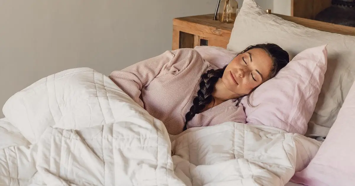 Woman sleeping peacefully in bed with white comforter and pink pillows in a cozy bedroom