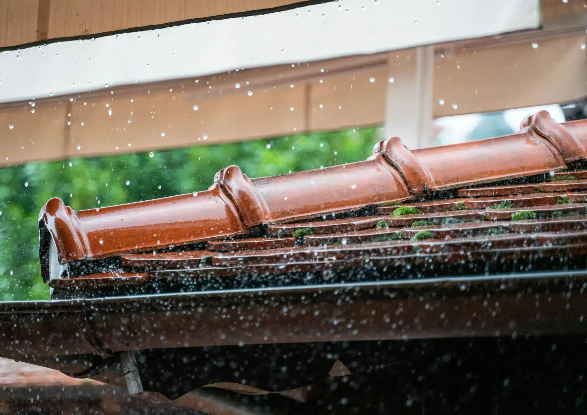 Raindrops falling on ceramic roof tiles with moss under a cloudy sky
