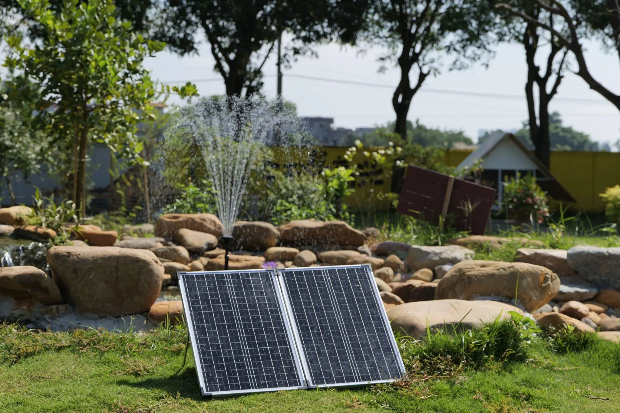 Solar panels on grass with water fountain and rocks in sunny garden setting