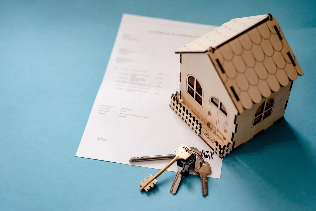 Wooden house model and keys on document over blue background
