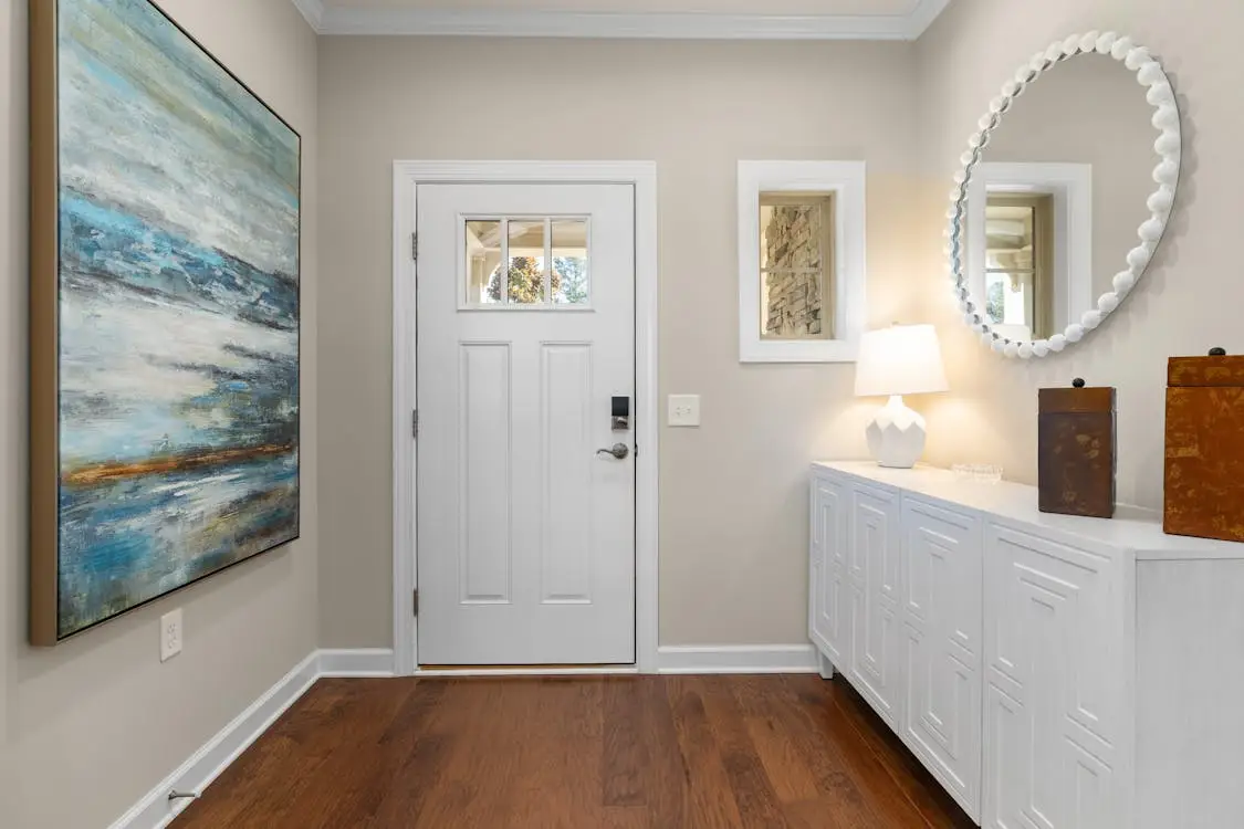 Contemporary entryway with white door, wooden floor, abstract painting, and decorative mirror on wall