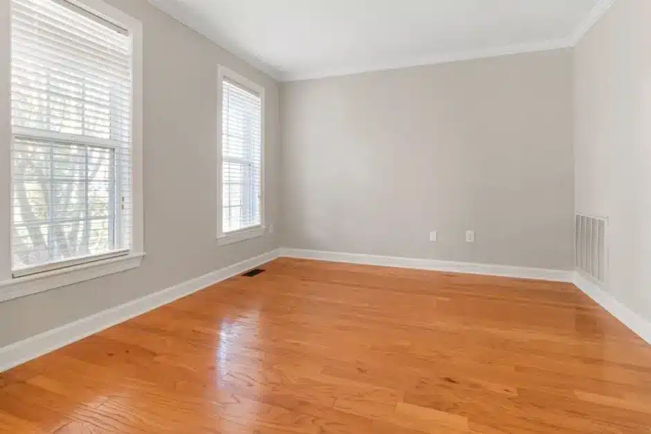 Empty room with hardwood floor, beige walls, and two large windows with blinds