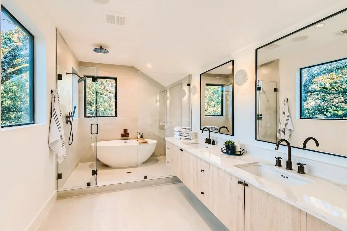Modern bathroom with freestanding tub, glass shower, and dual sinks under soft natural light