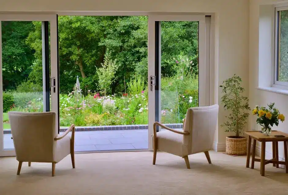 Two beige chairs facing garden view through glass doors in bright living room