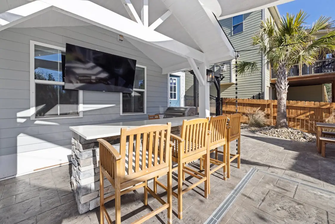 Outdoor patio with wooden chairs and stone bar, large TV mounted on house wall