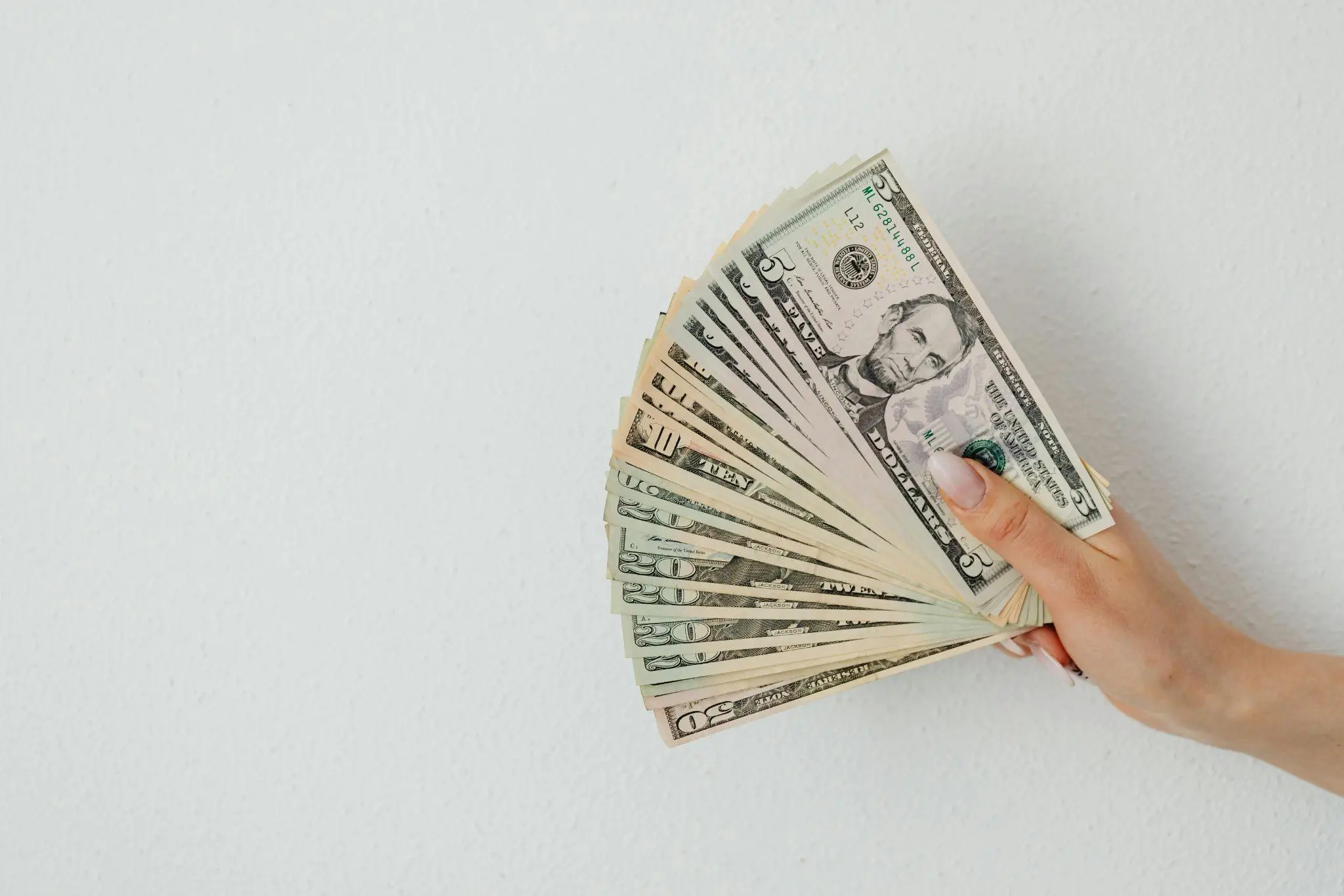 Hand holding a fan of US dollar bills against a white textured background