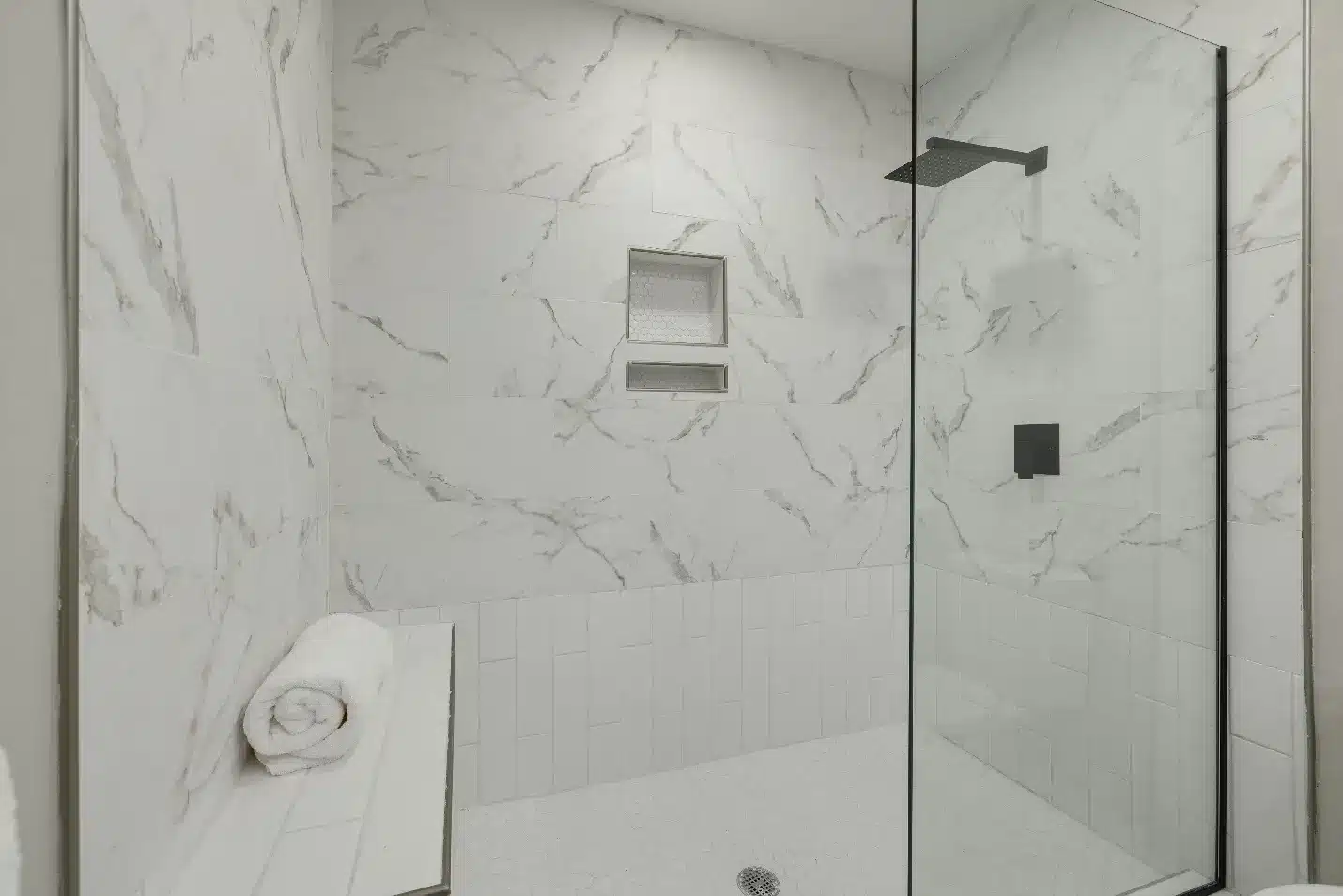 Marble tile shower with glass door and rain showerhead in modern bathroom setting