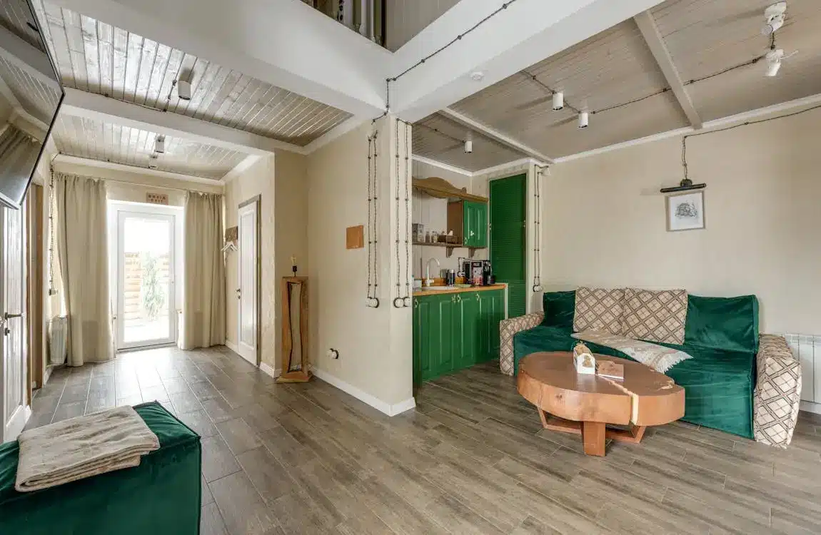 Spacious living room with green sofa, wooden coffee table, and kitchenette with green cabinets