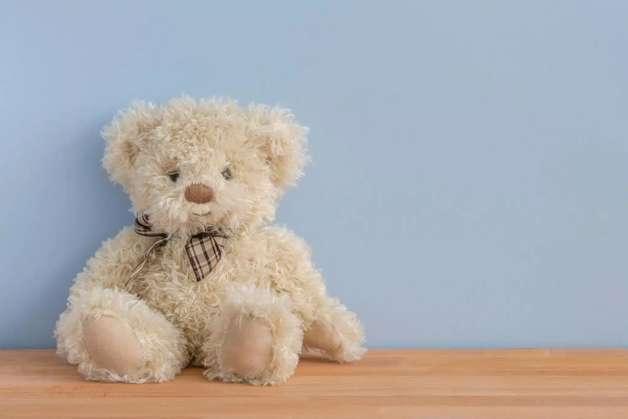 Fluffy teddy bear with plaid bow tie on wooden surface against light blue wall