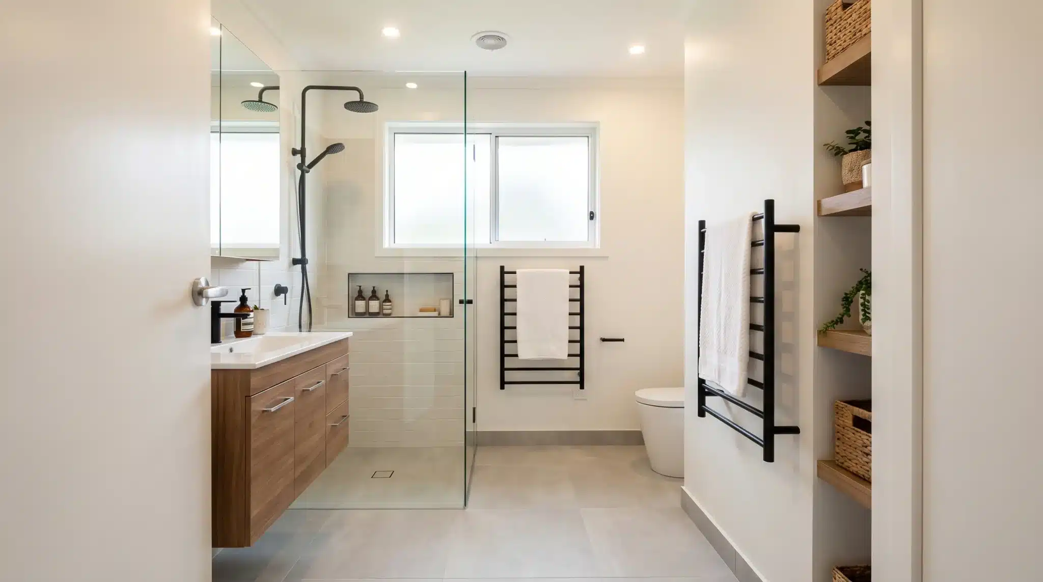 Modern bathroom with wooden vanity, glass shower, and towel rack in bright natural light