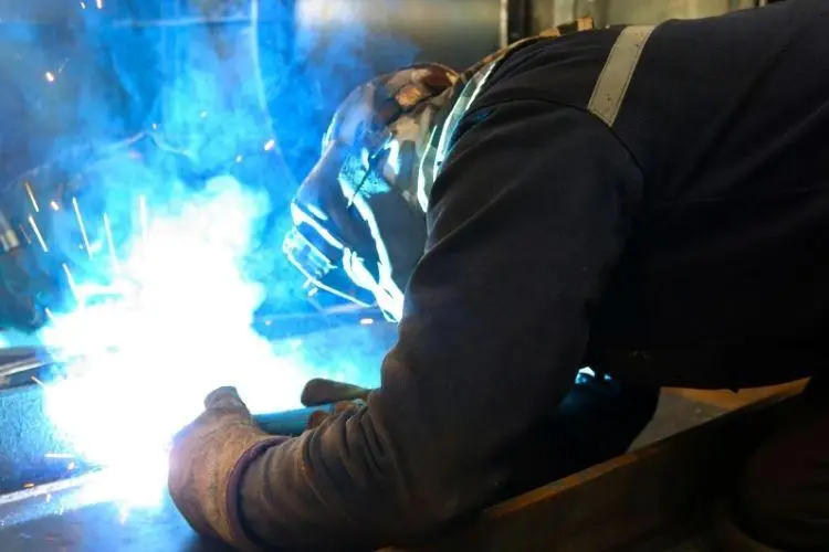 Welder in protective gear working indoors with bright blue welding sparks