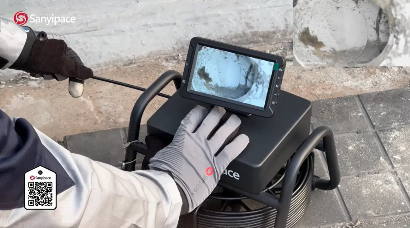 Technician using inspection camera equipment to examine pipe interior on concrete surface