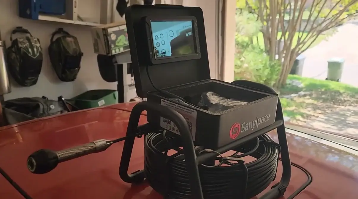 Inspection camera with coiled cable and monitor on red car hood in garage setting