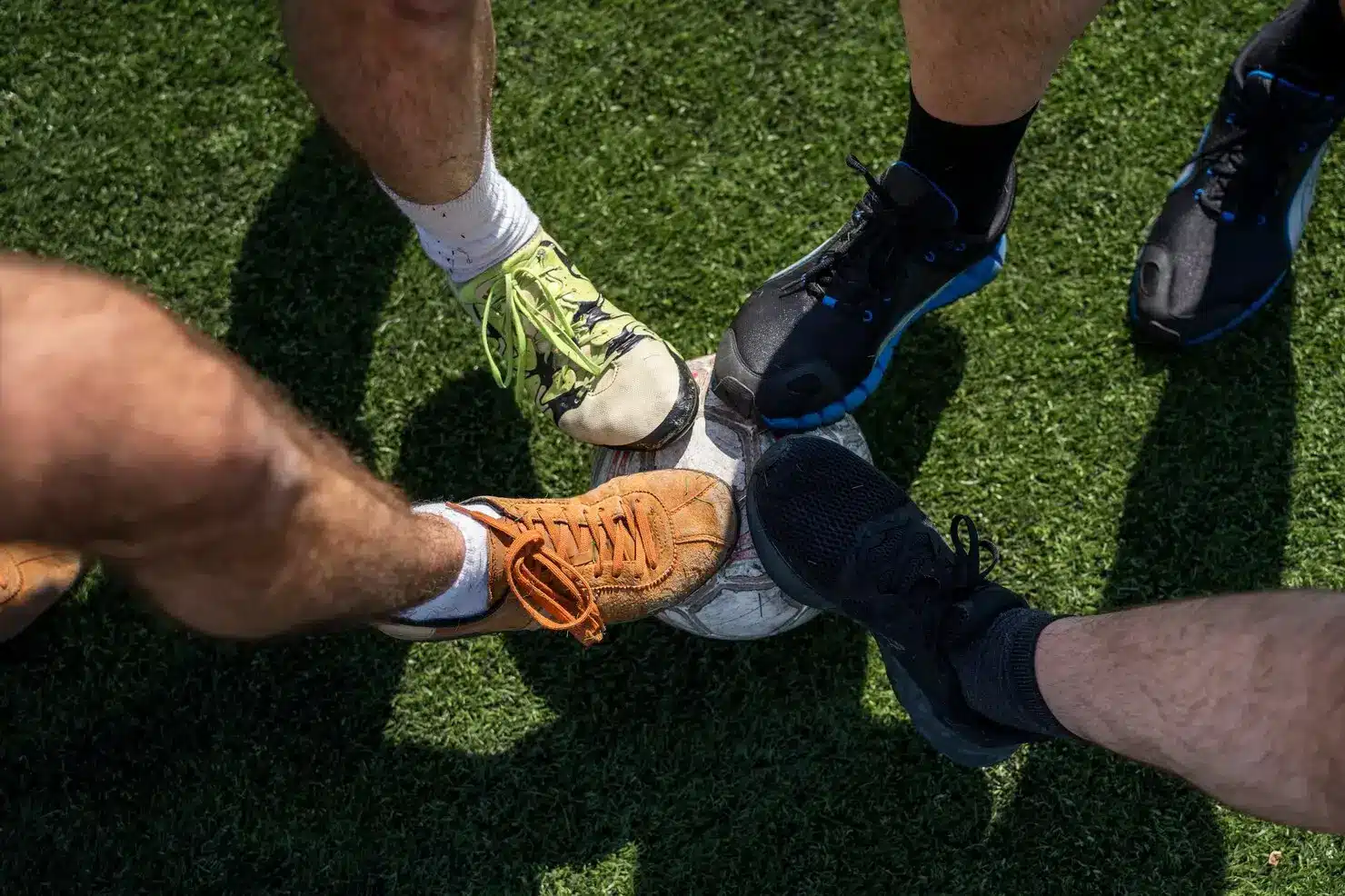 Four colorful shoes surrounding a soccer ball on green grass field