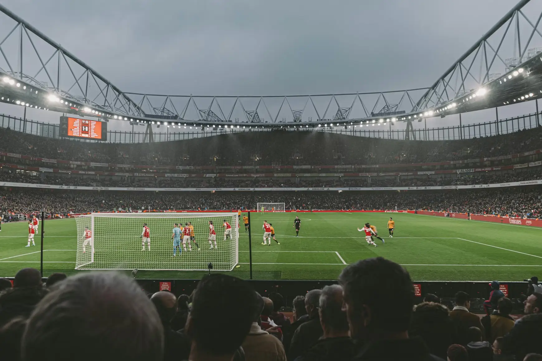 Soccer match in stadium with players gathered near goalpost under overcast sky