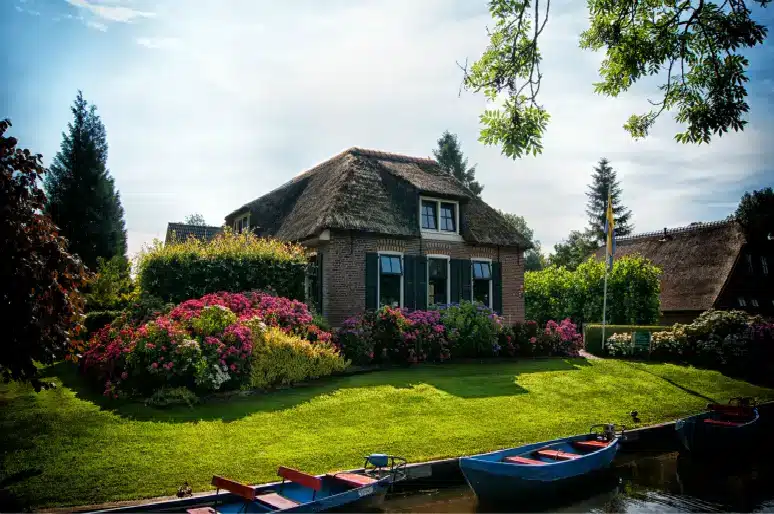Thatched-roof cottage with blooming garden by calm waterway under clear sky
