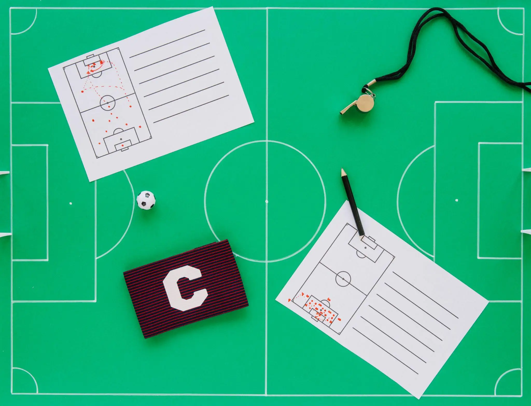 Soccer field strategy papers, whistle, and captain's armband on green pitch board