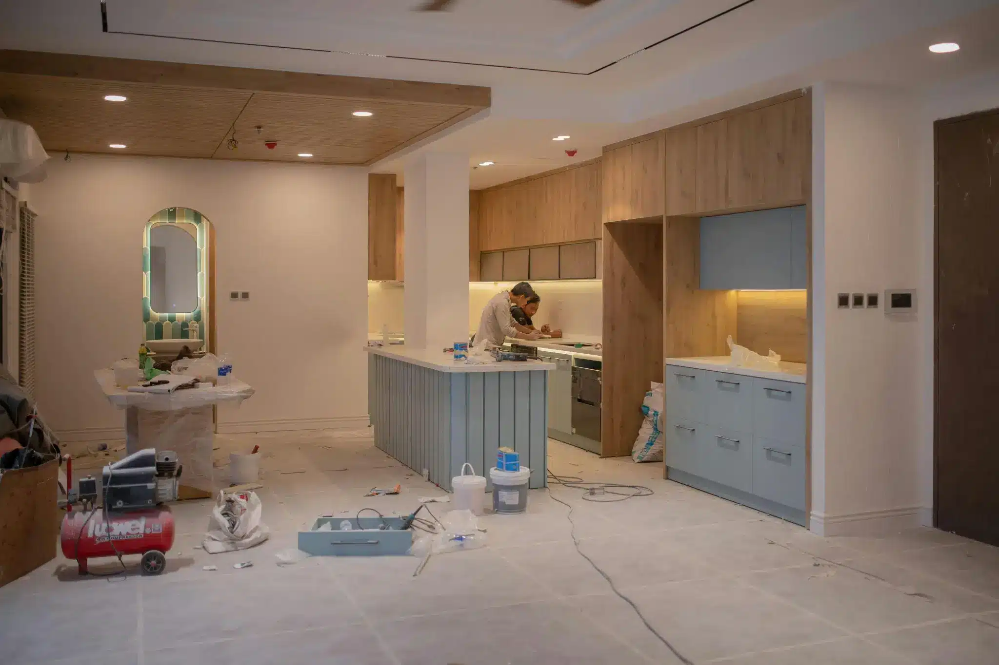 Man working on kitchen renovation with wooden cabinets and under-counter lighting